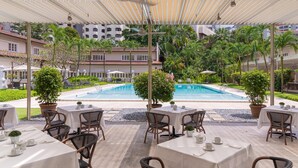 An outdoor pool area with tables and chairs, surrounded by greenery and buildings in the background. - Goodwood Park Hotel (Singapore)