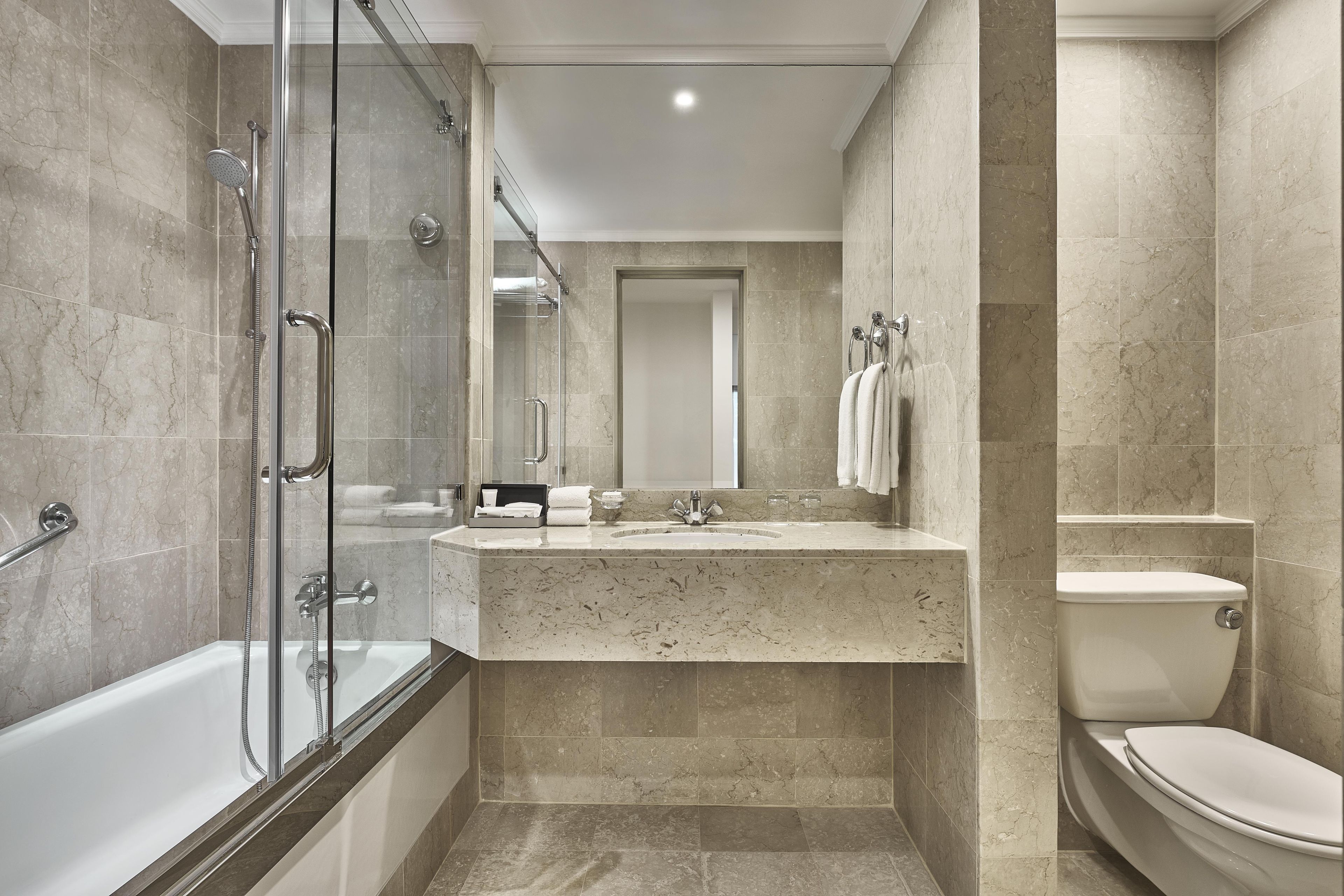 Un baño moderno con ducha de vidrio, bañera independiente, tocador con azulejos de mármol y un inodoro.