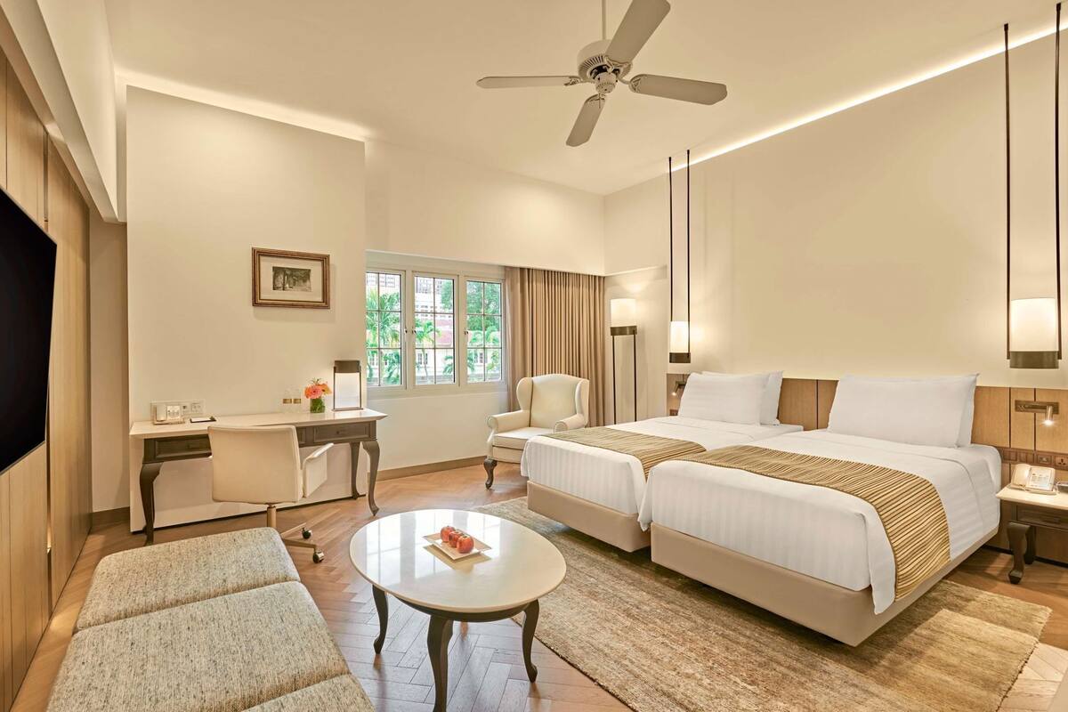 Habitación de hotel con dos camas, un escritorio, una silla, un televisor y un ventilador de techo.