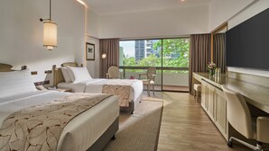 A hotel room with two beds, a desk, a chair, a TV, and a balcony with a view of buildings and greenery. - Goodwood Park Hotel (Singapore)