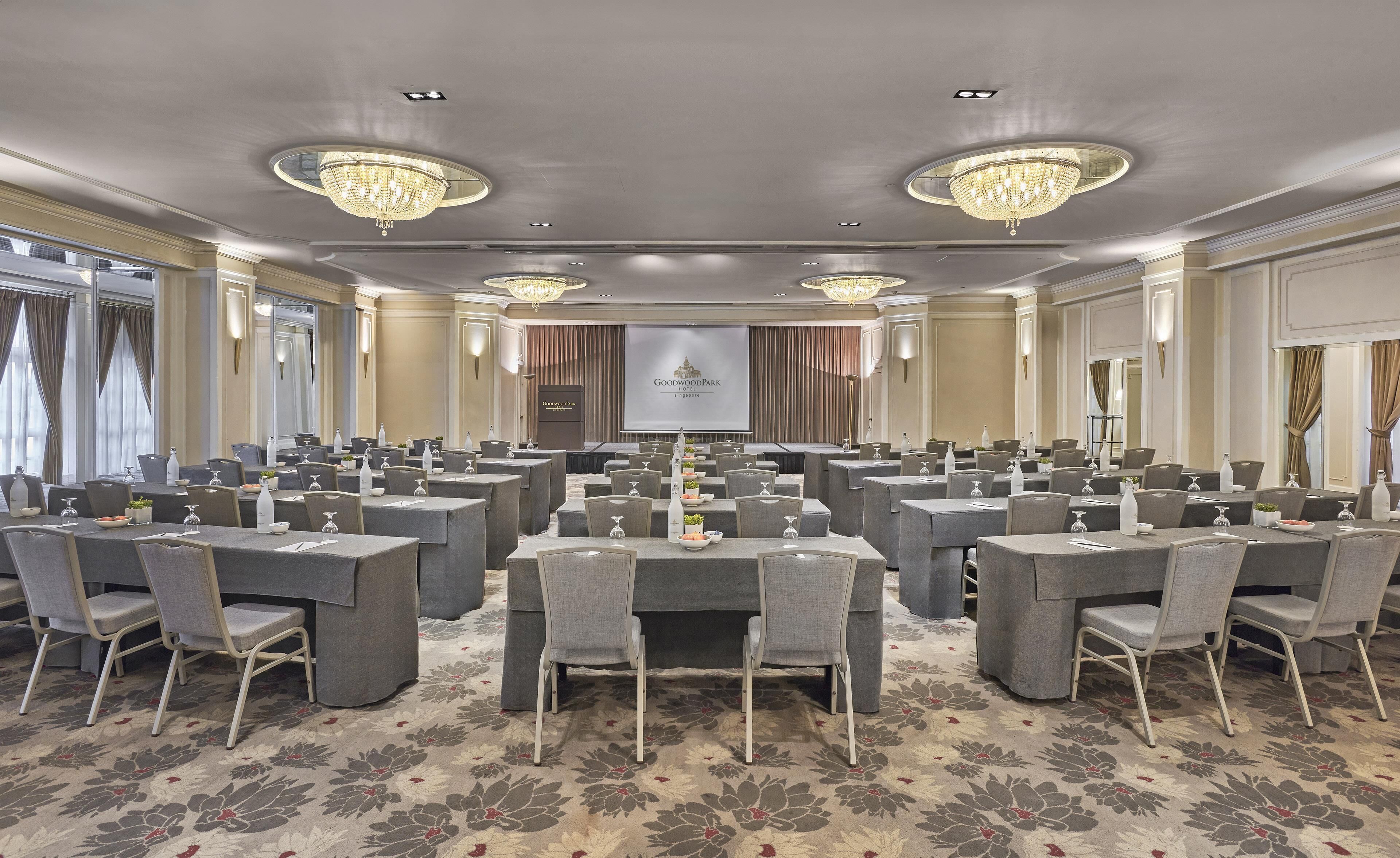 Un salón de conferencias con mesas redondas, sillas y una pantalla grande que muestra el nombre del hotel.
