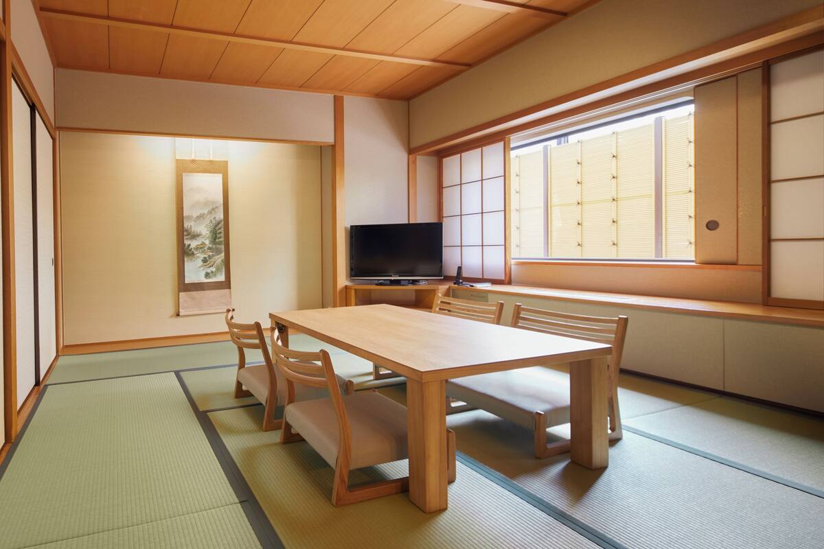 Une pièce de style japonais traditionnel, avec un sol recouvert de tatamis, une table basse, des chaises, un téléviseur et des portes coulissantes.