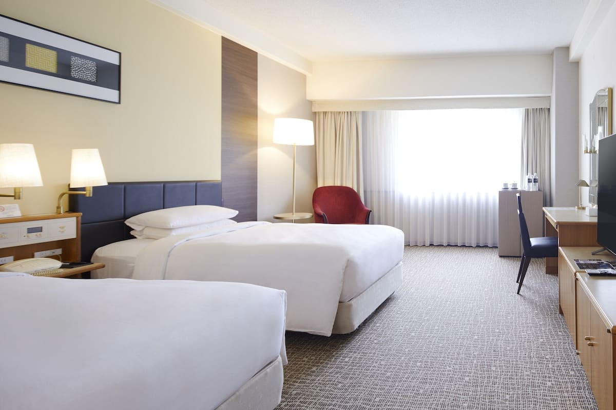 Une chambre d’hôtel avec deux lits, un bureau, une chaise et un téléviseur.