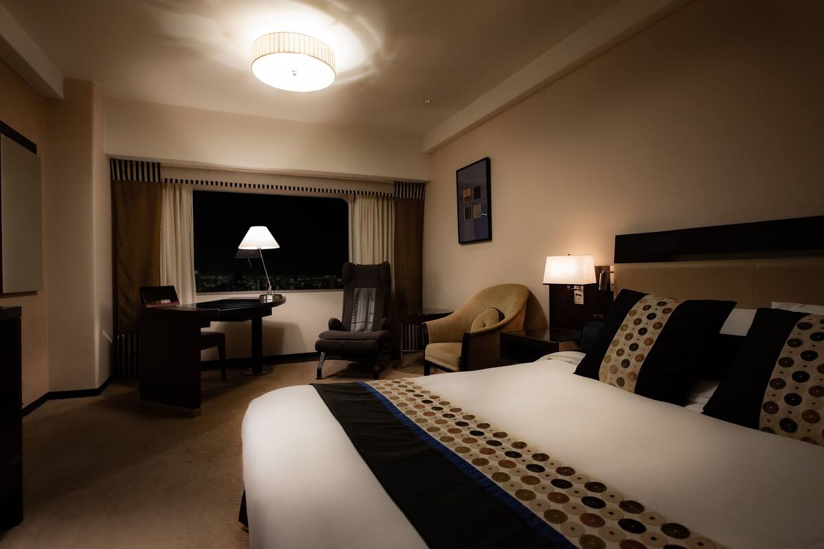 Une chambre d’hôtel avec un grand lit, un bureau, une chaise et une fenêtre avec des rideaux.