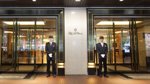 L’entrée d’un hôtel, avec deux employés en uniforme qui se tiennent devant.