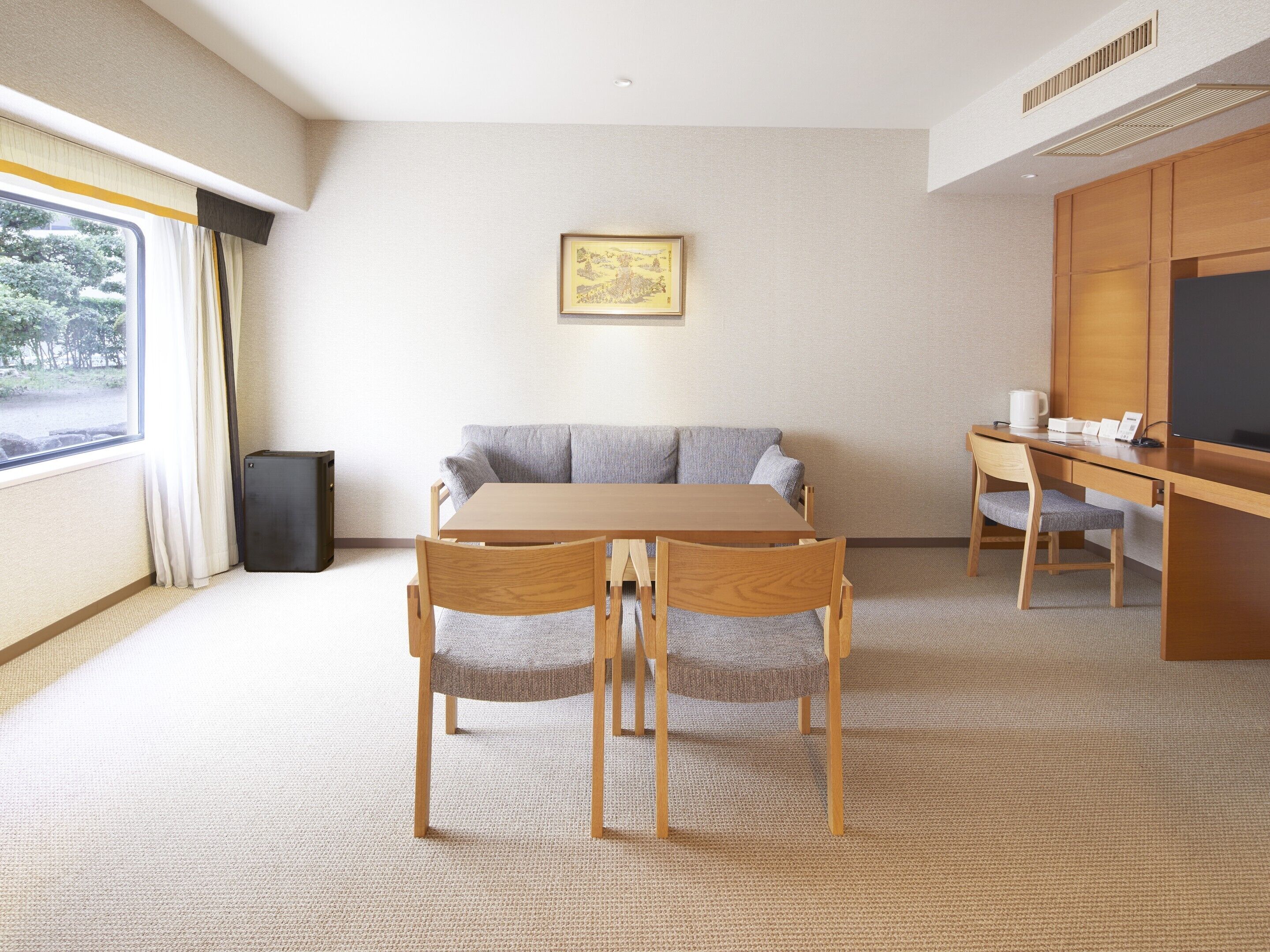 A hotel room with a wooden table, two chairs, a sofa, a TV, and a small speaker.