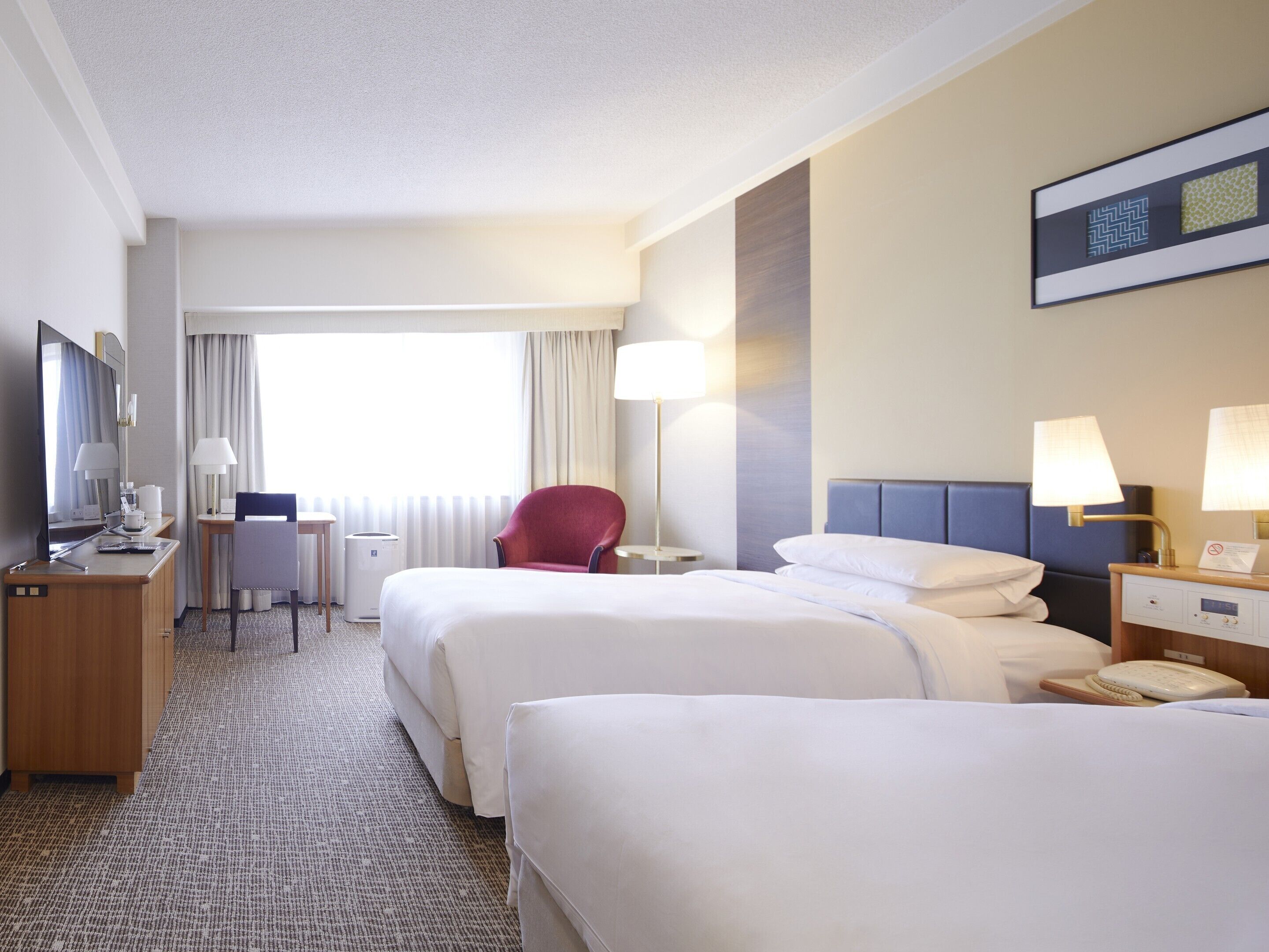 A hotel room with two beds, a desk, a chair, a TV, and a window with curtains.