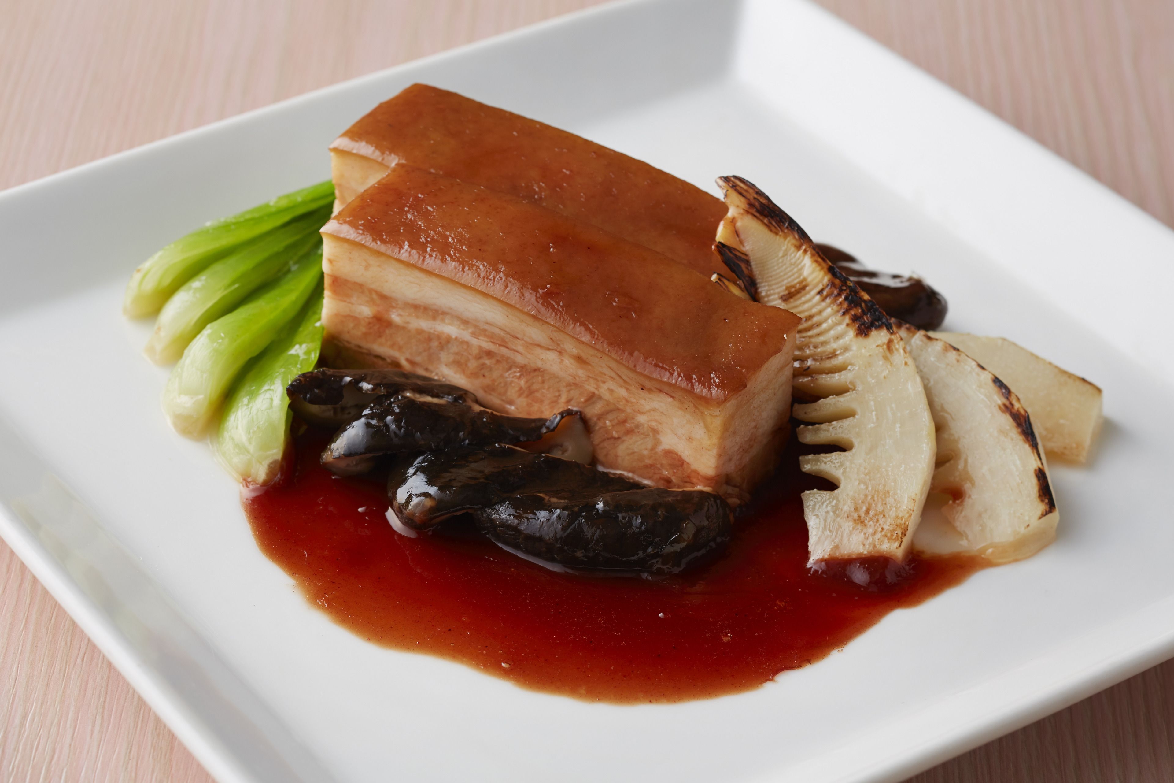 A plate with a glazed pork belly, bok choy, and grilled mushrooms.