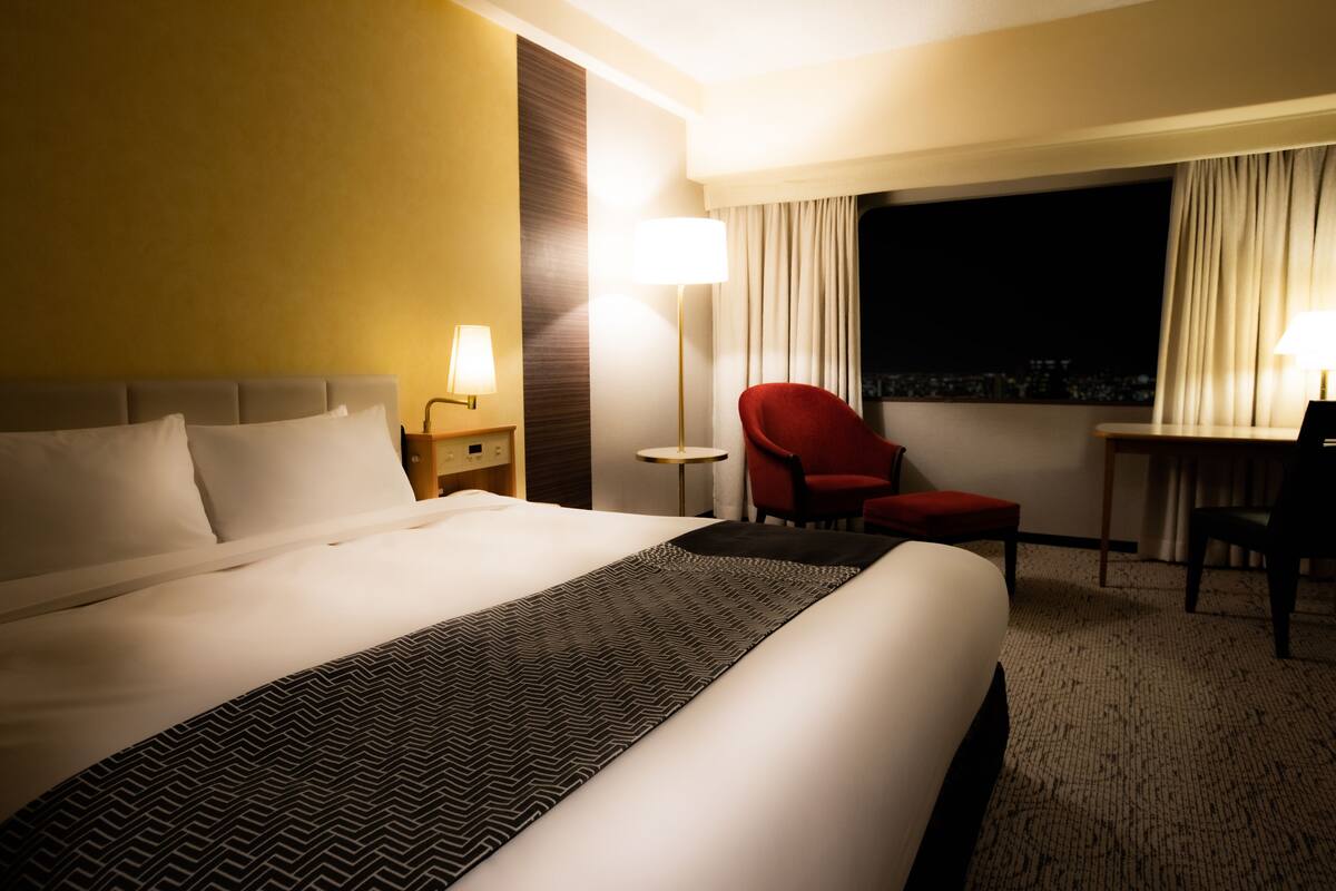Une chambre d’hôtel avec un grand lit, un fauteuil rouge, un bureau et une lampe.