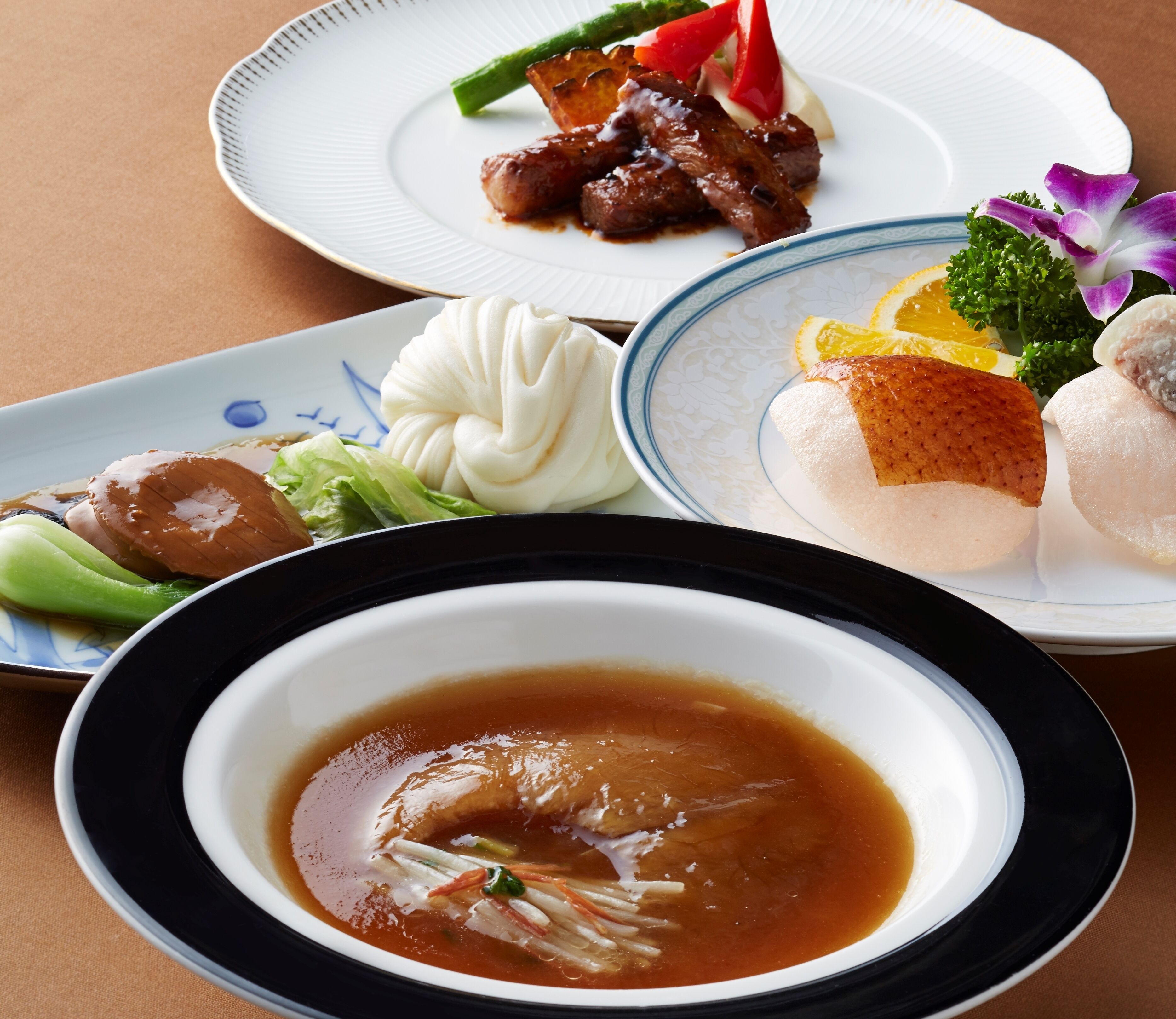 A table with various dishes including a bowl of soup, a plate with meat, vegetables, and dumplings.