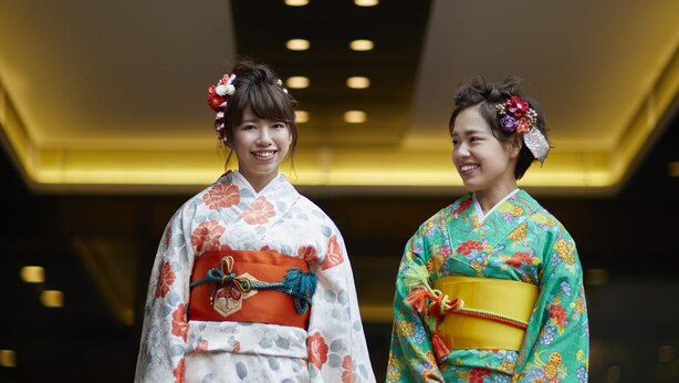 Deux personnes, vêtues de kimonos traditionnels japonais, se tiennent devant un bâtiment sur lequel on peut lire l’inscription « The New Otani ».