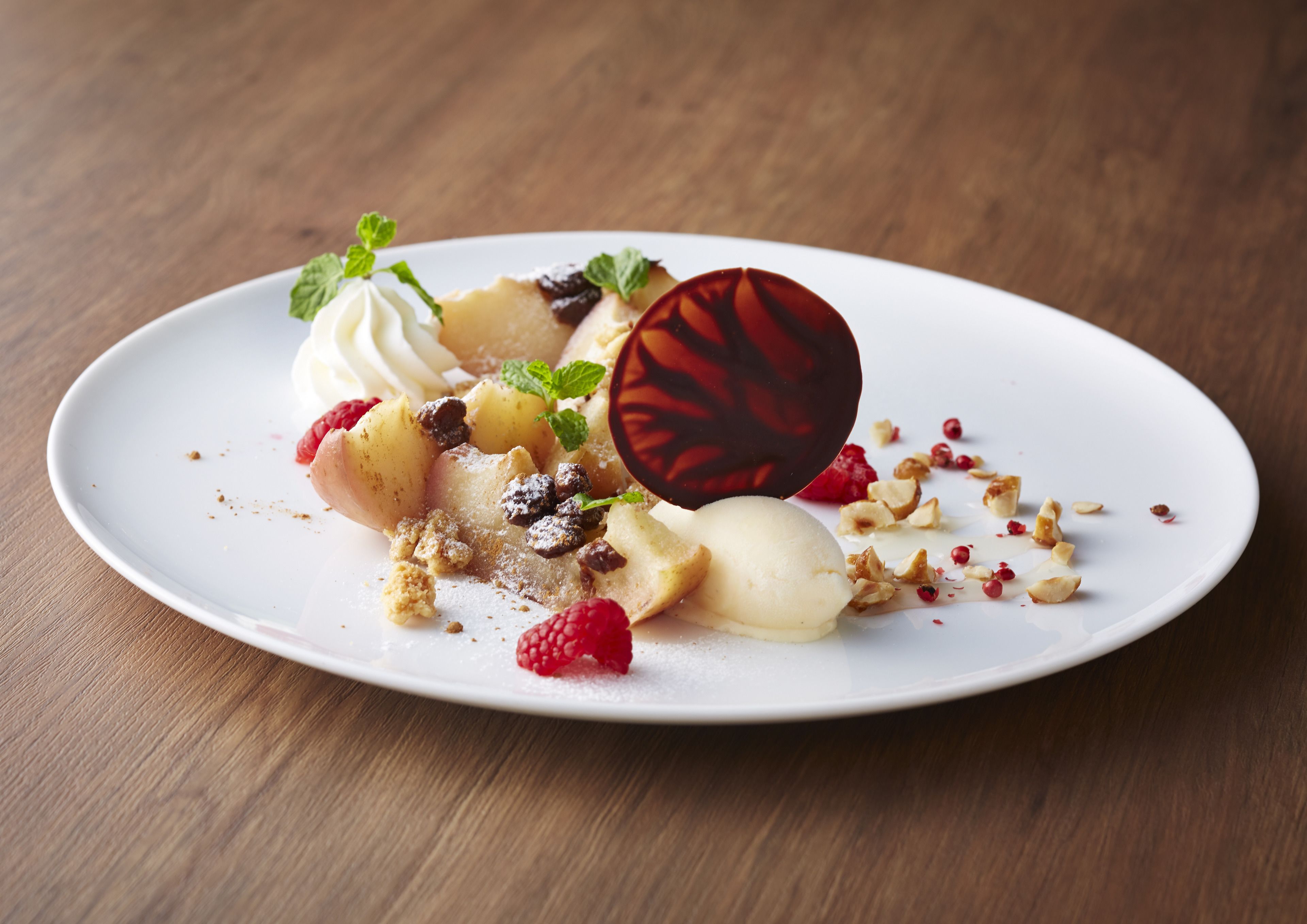 Un dessert servi dans une assiette blanche, composé de framboises, d’une boule de glace et d’une sphère de chocolat.