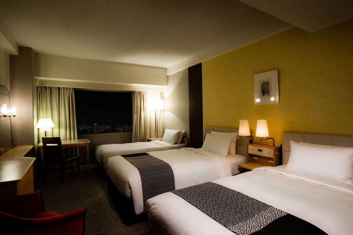 Une chambre d’hôtel avec deux lits, un bureau, une chaise et une table de chevet avec des lampes.