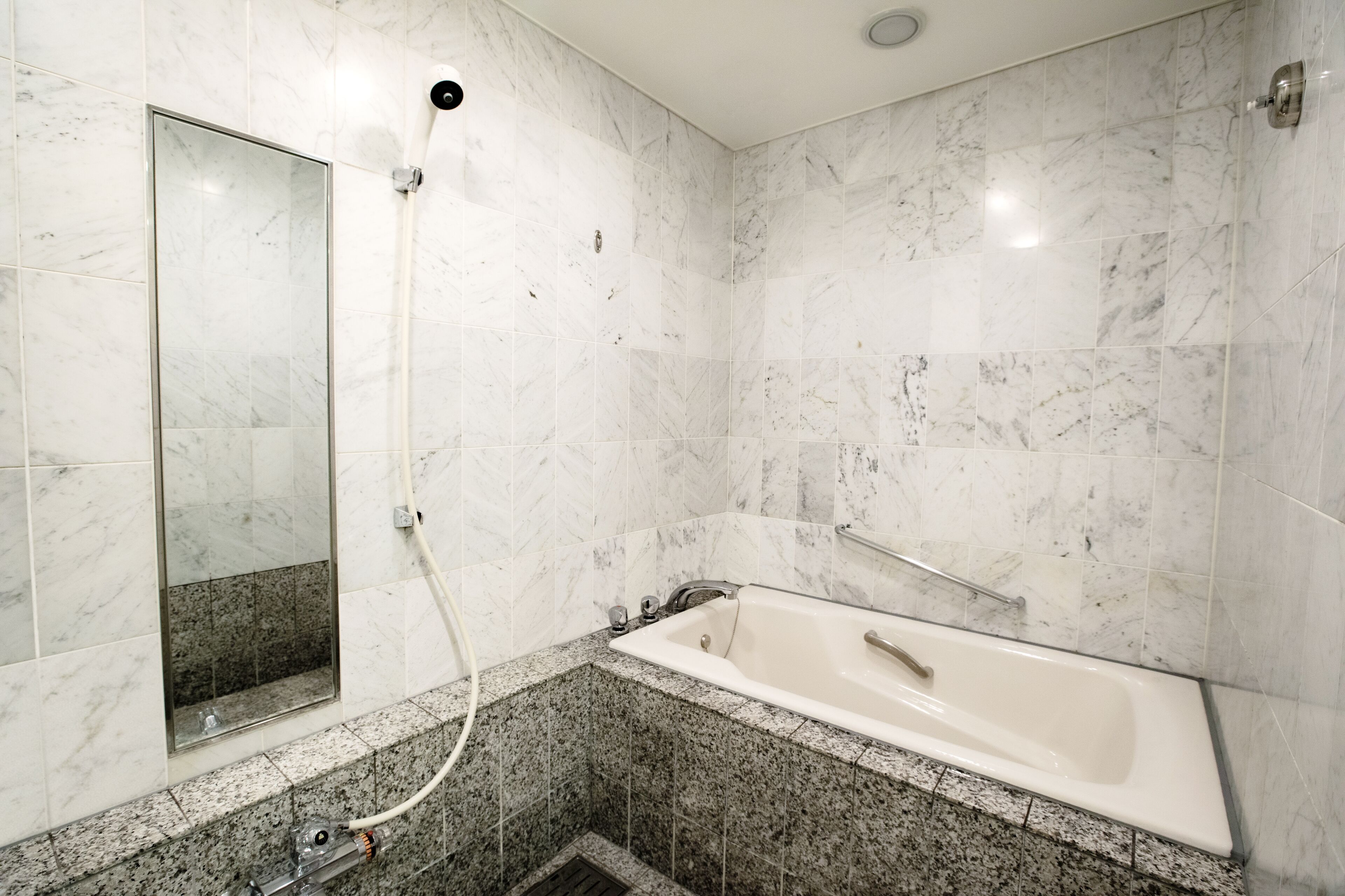 A bathroom with a marble shower, a bathtub, and granite countertops.