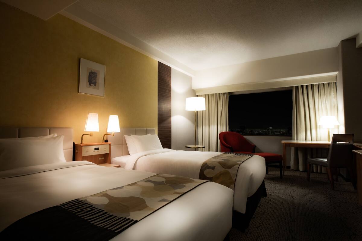 Une chambre d’hôtel avec deux lits, un bureau, une chaise et une table de chevet avec des lampes.