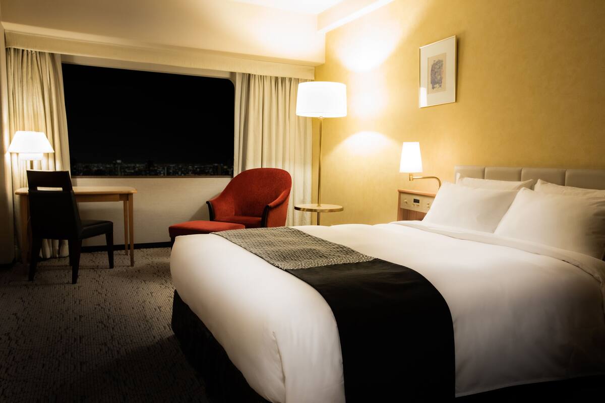 Une chambre d’hôtel avec un grand lit, un bureau, une chaise et une table de chevet avec des lampes.