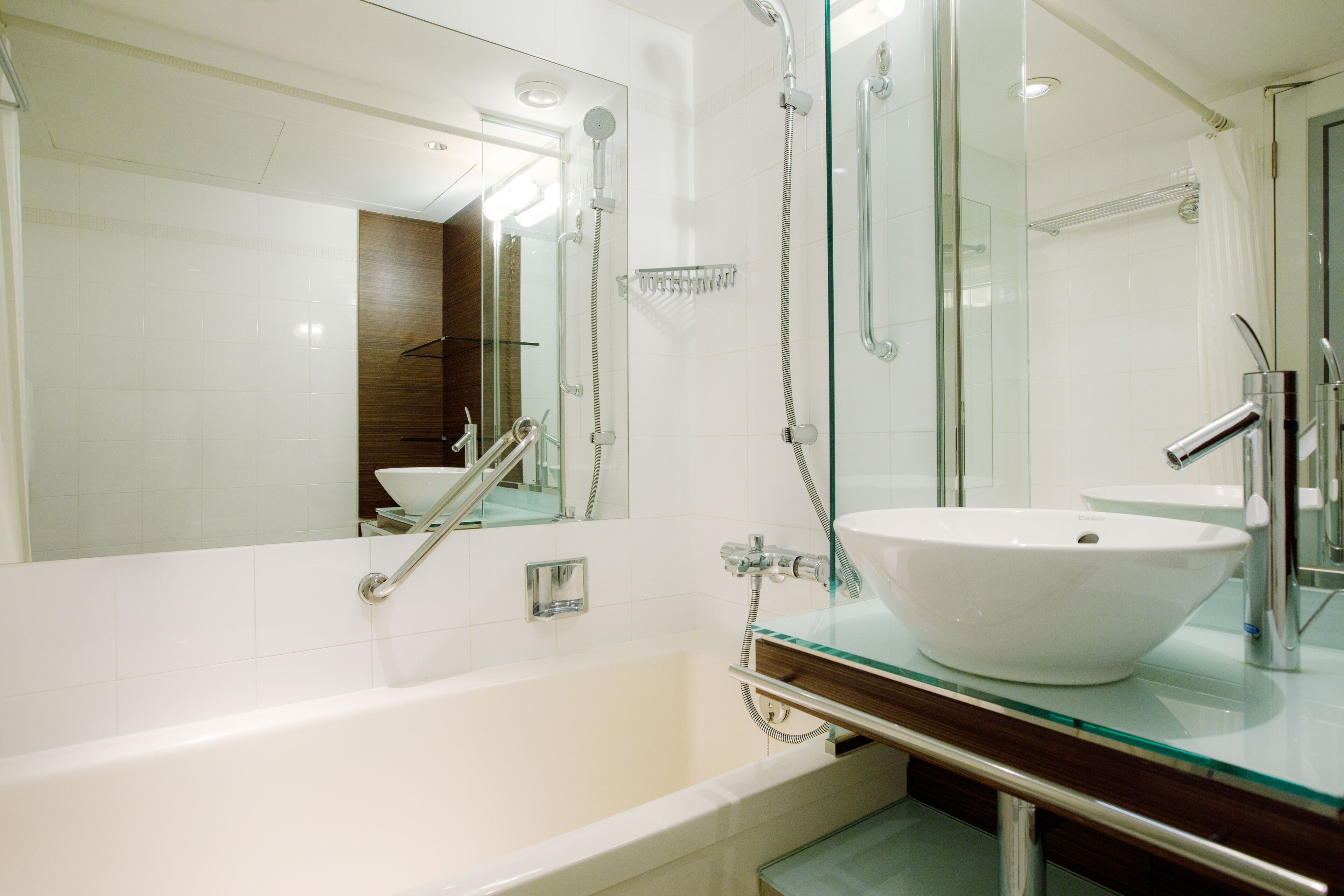 A modern bathroom with a glass-enclosed shower, a white bathtub, and a glass sink.