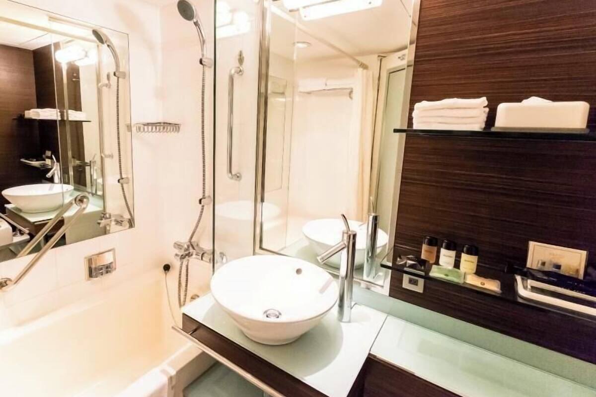 Une salle de bain moderne avec un grand miroir, un lavabo rond, une douche et des toilettes séparées par une paroi de verre.