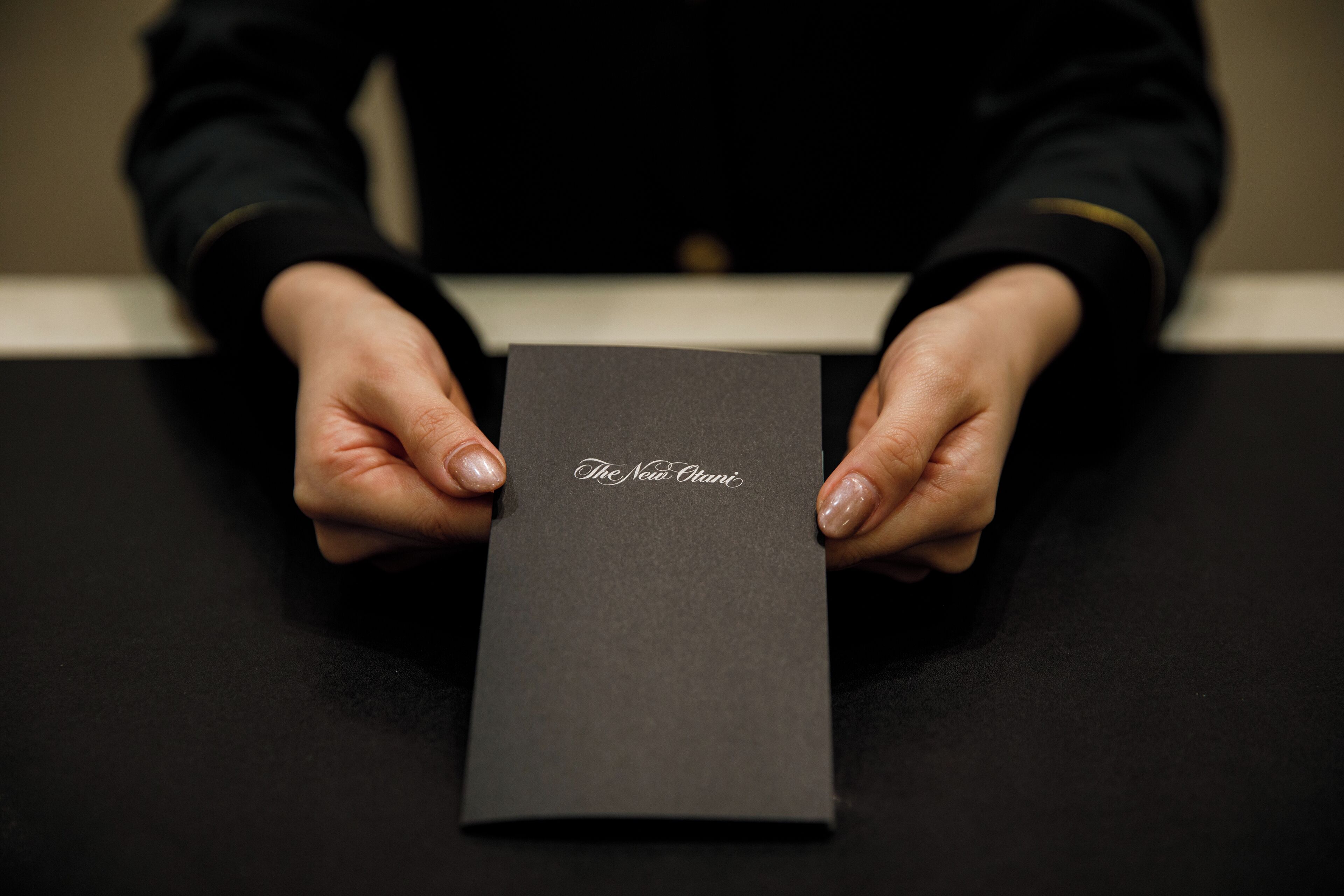 A person holding a black box with the text "The New Otani" on it.