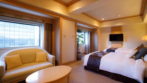 Une chambre d’hôtel avec un canapé, un lit, une télévision et une fenêtre avec des stores.