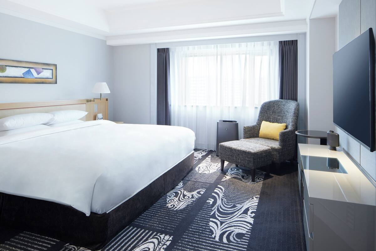 Une chambre d’hôtel avec un grand lit, une chaise, une télévision et une fenêtre avec des rideaux.