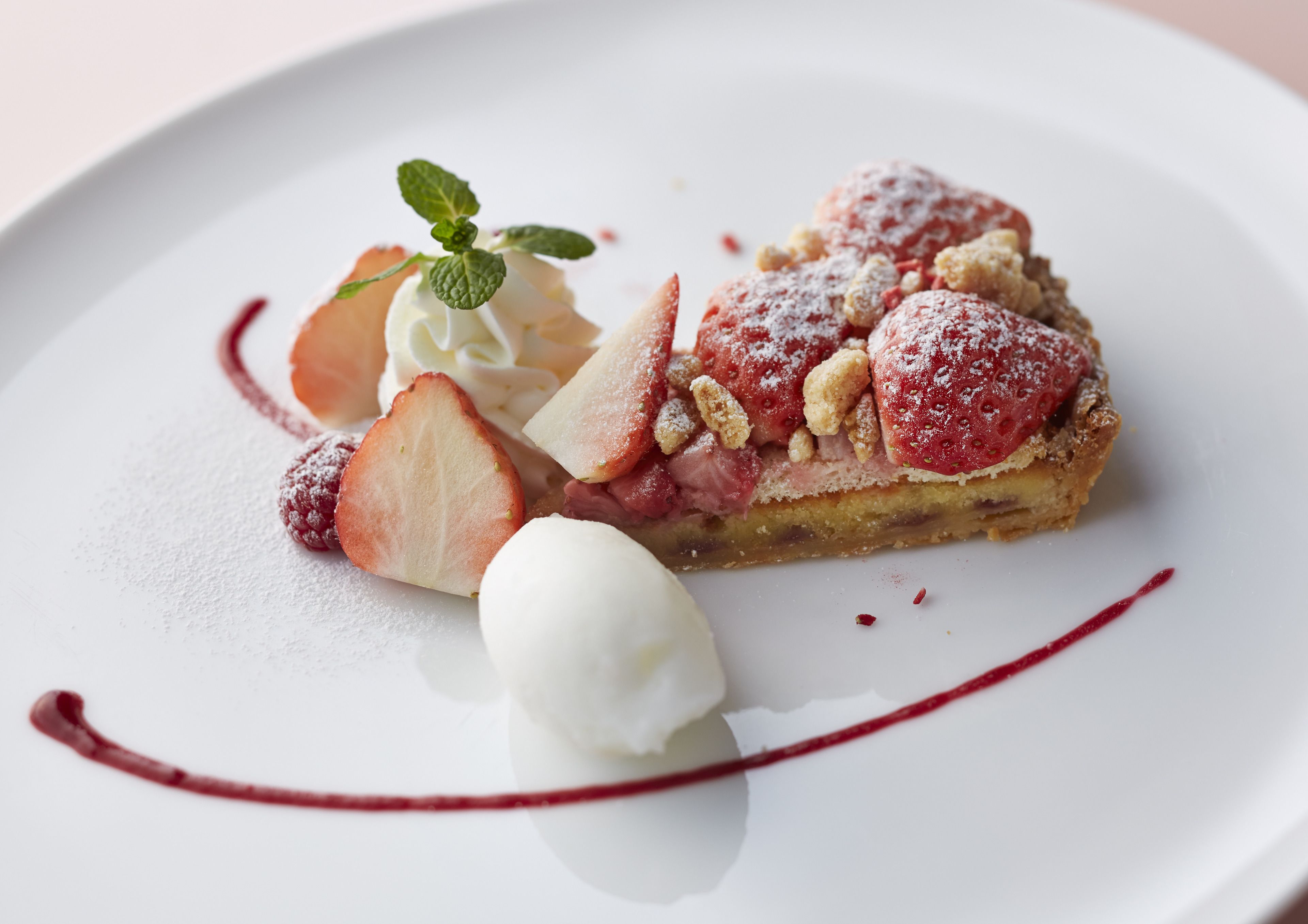 A dessert plate with a slice of pie, strawberries, whipped cream, and a mint garnish.