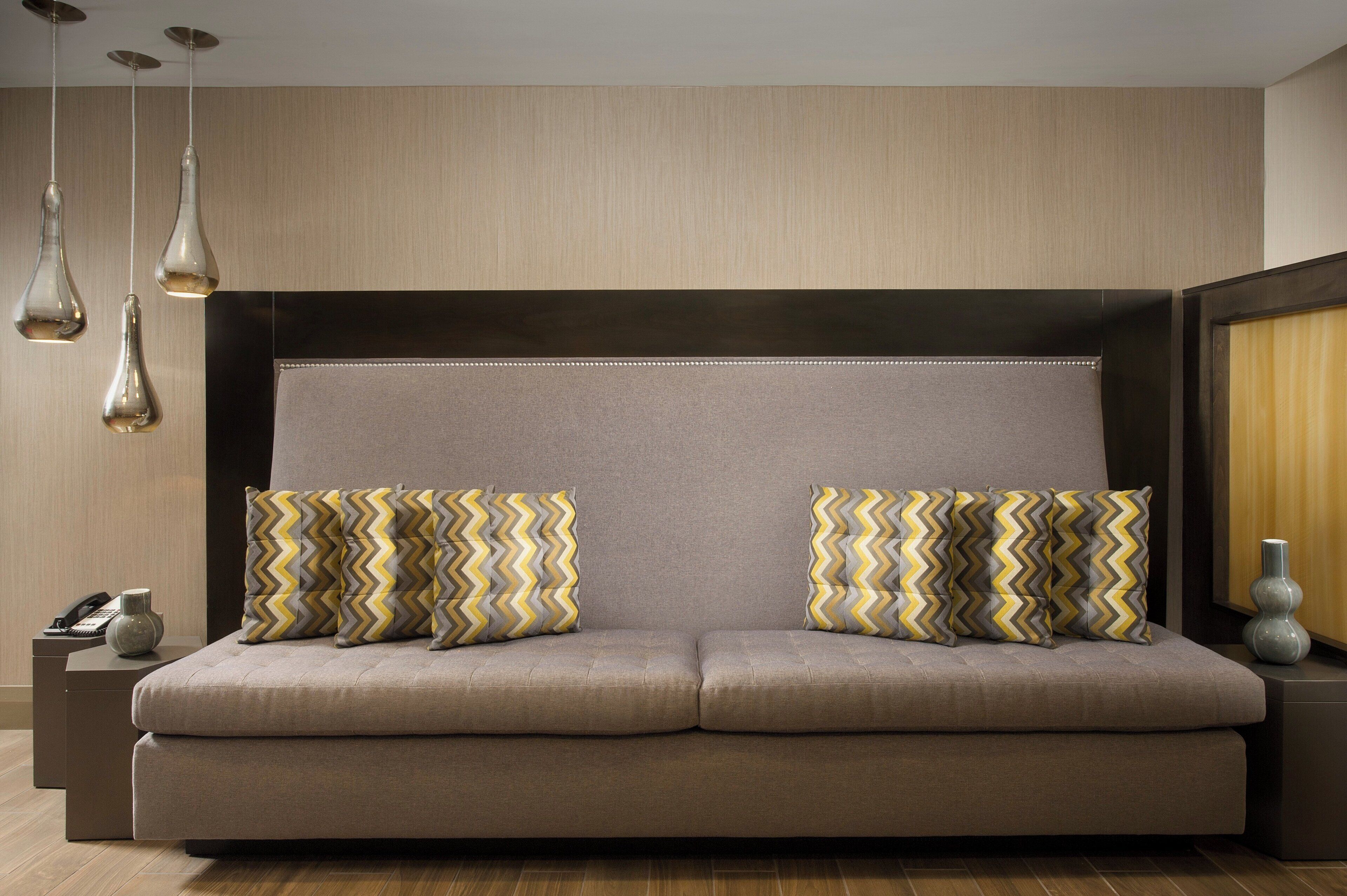 A modern sofa with two matching pillows, a small bedside table, a vase, and pendant lights.