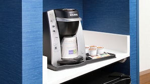 A Keurig coffee machine with a coffee pod holder and a tray with coffee cups.