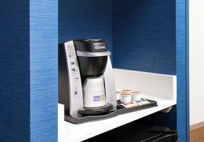 Una cafetera Keurig con un portacapsulas de café y una bandeja con tazas de café.
