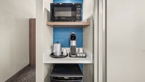 A kitchenette with a microwave, coffee machine, and trash bin.