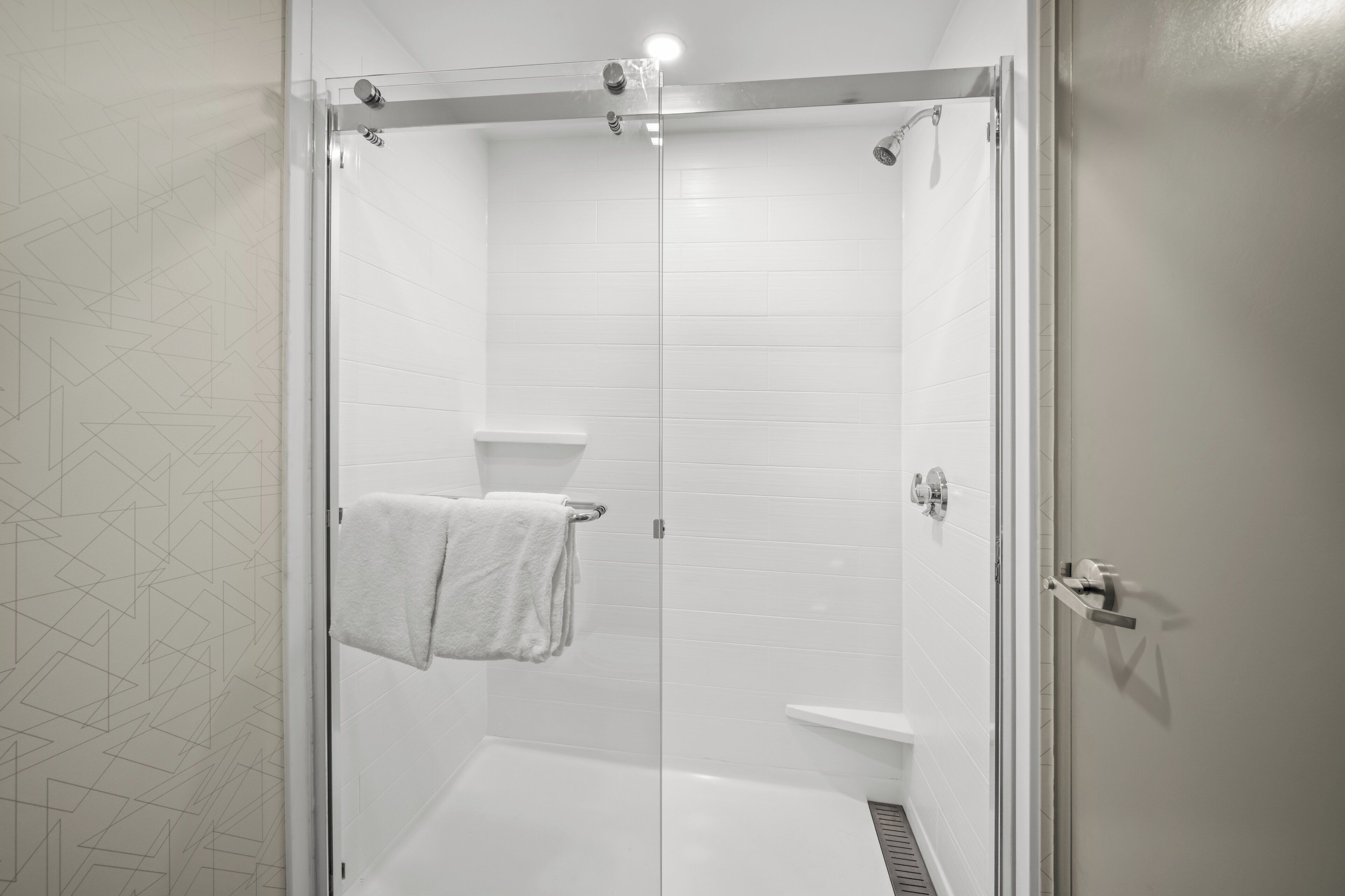 A modern shower with a glass door, a white tiled wall, and a towel hanging on the door handle.