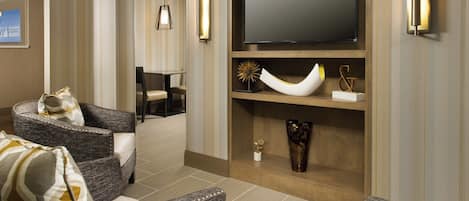 A hotel lobby with a seating area, a flat-screen TV mounted on a wooden wall, and a reception desk.