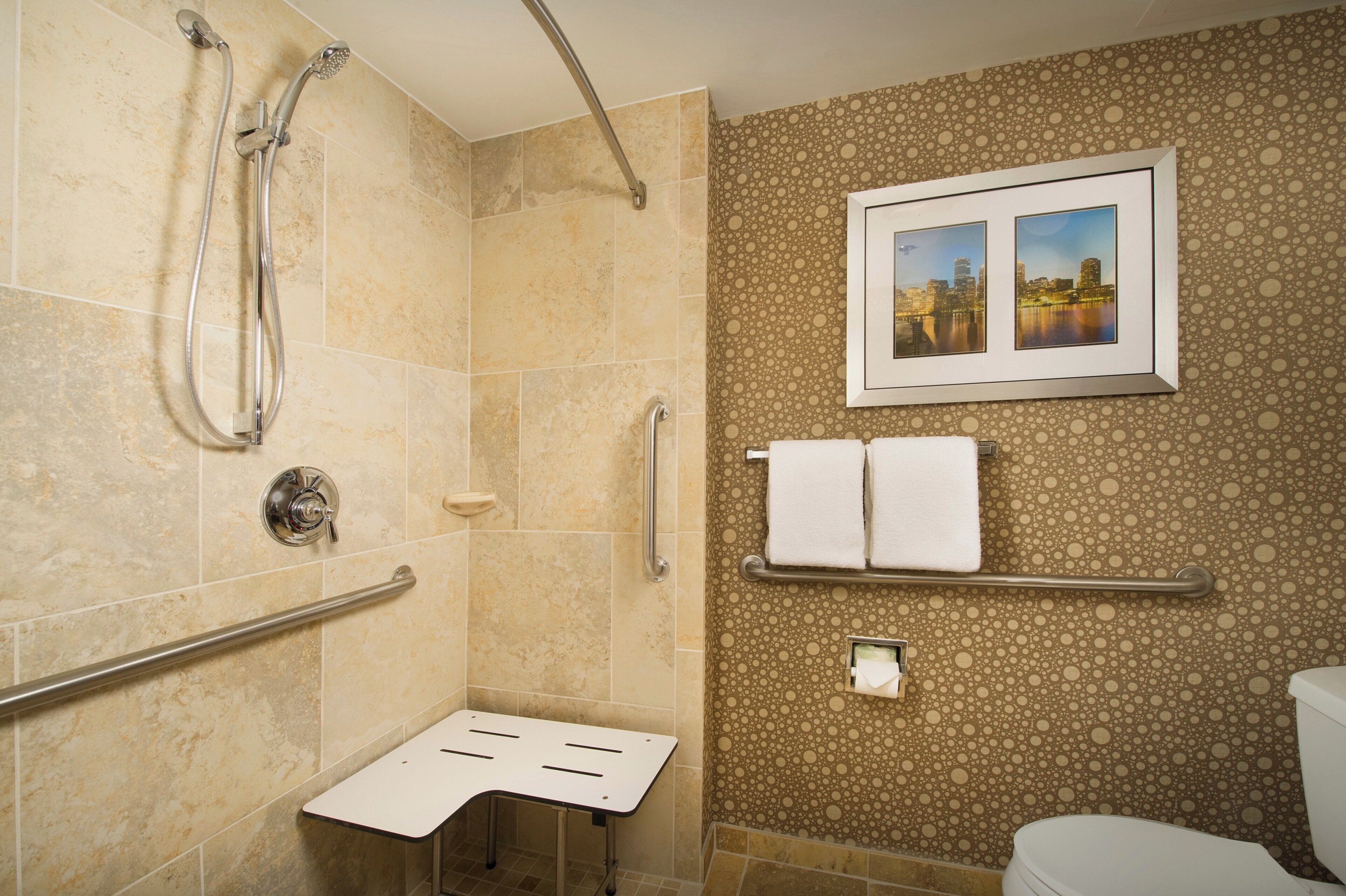 A bathroom with a shower, grab bars, a toilet, and a wall-mounted sink.