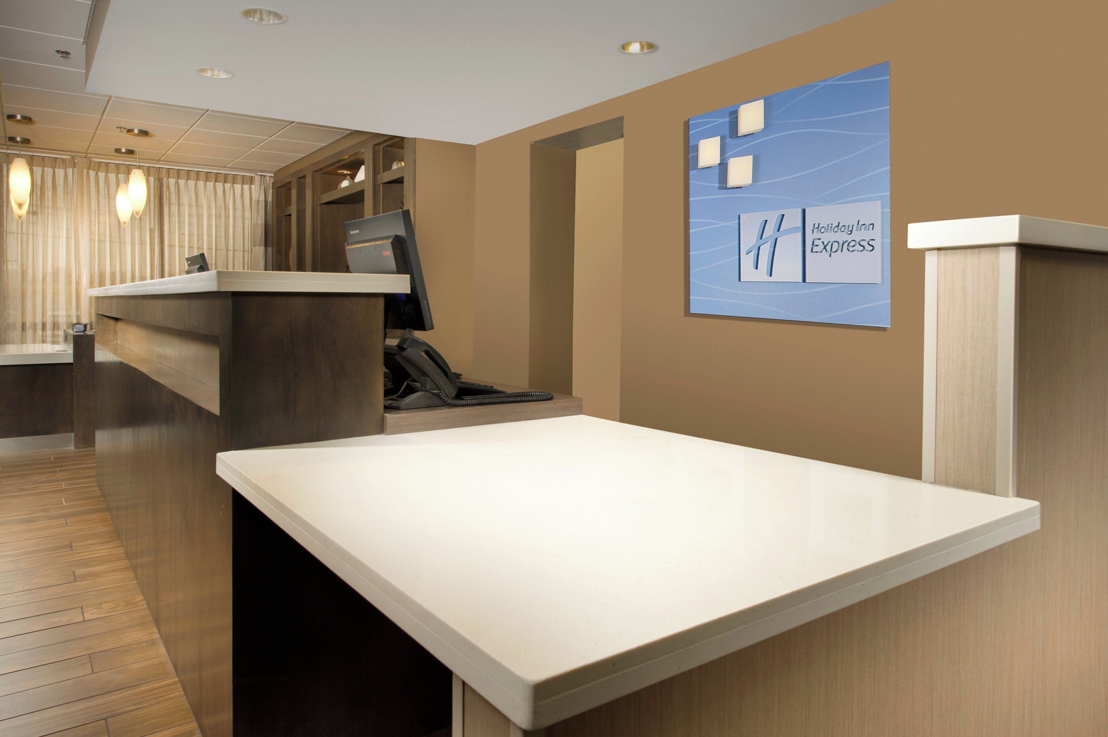 A hotel reception desk with a computer, phone, and a wall-mounted sign for Holiday Inn Express.