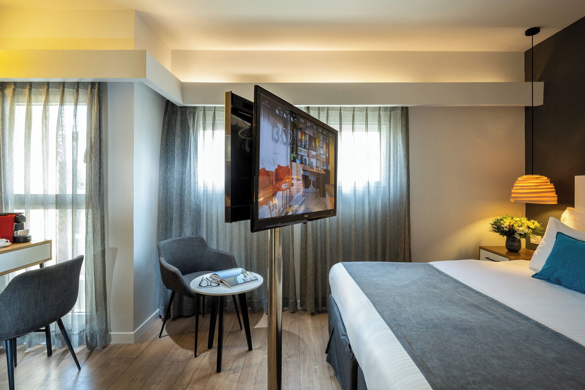 Una habitación de hotel con cama, escritorio y silla, televisor sobre un mueble y lámpara.