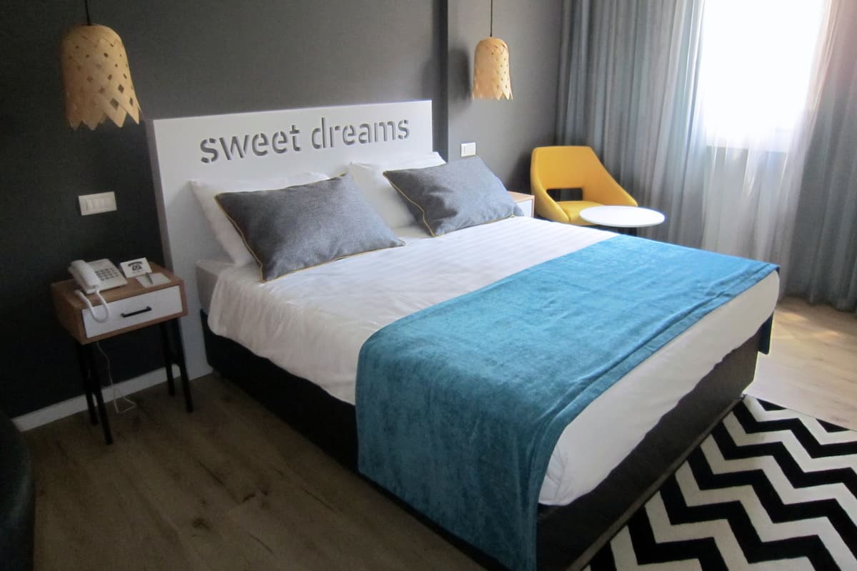 Une chambre d’hôtel moderne avec un grand lit, un téléphone sur la table de chevet, une petite table et une chaise.