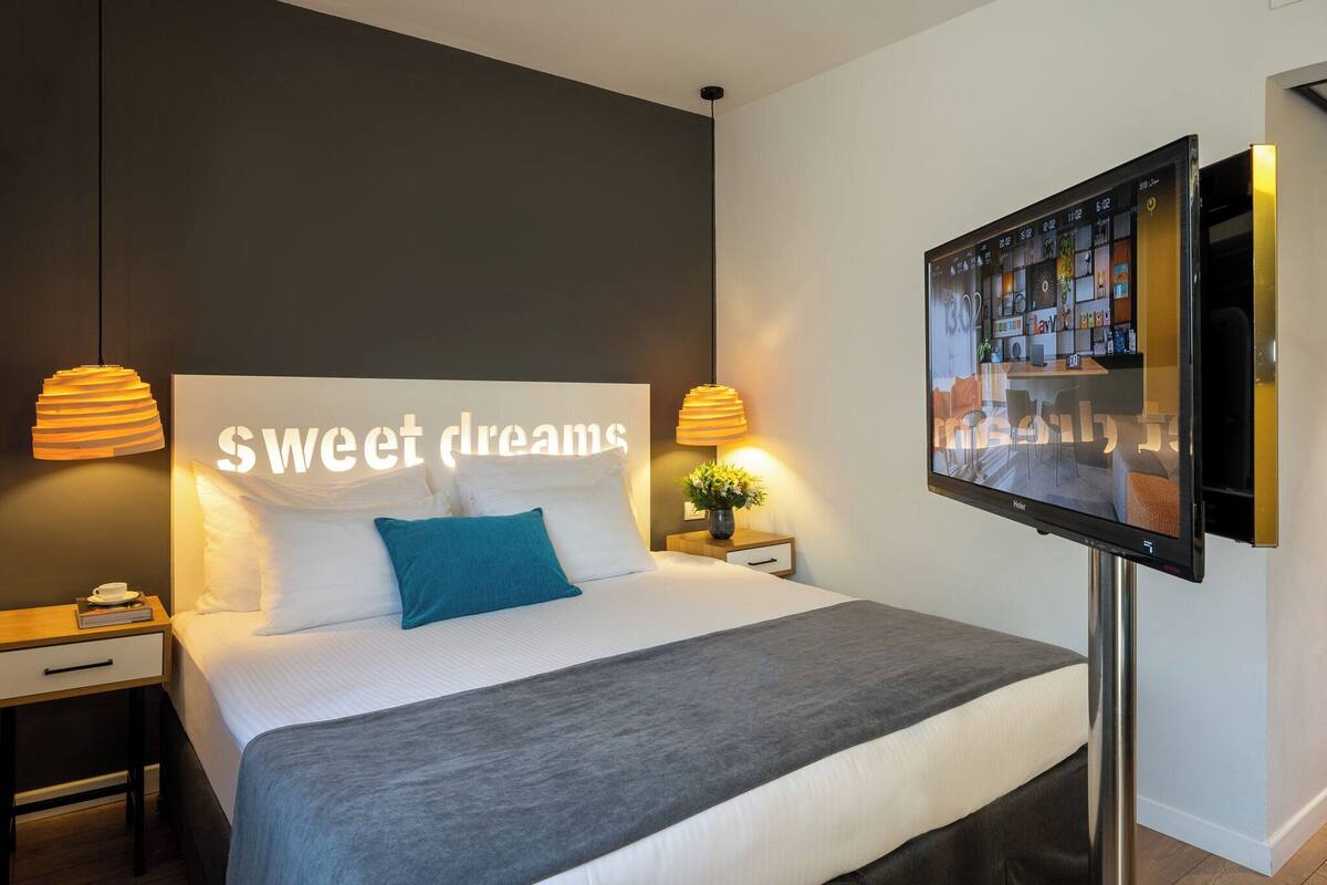 Une chambre d’hôtel avec un lit, une télévision, une table de chevet et un mur sur lequel est écrit « doux rêves ».