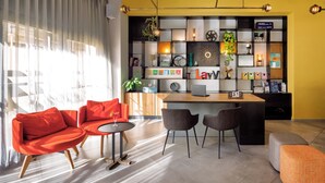 Uma sala de estar moderna com um sofá vermelho, uma mesa redonda pequena e duas cadeiras. Há uma área de cozinha com bancada de madeira e um laptop.