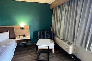 Ein Hotelzimmer mit Bett, Schreibtisch, Stuhl, Wandheizung und einem fenster mit Vorhängen.