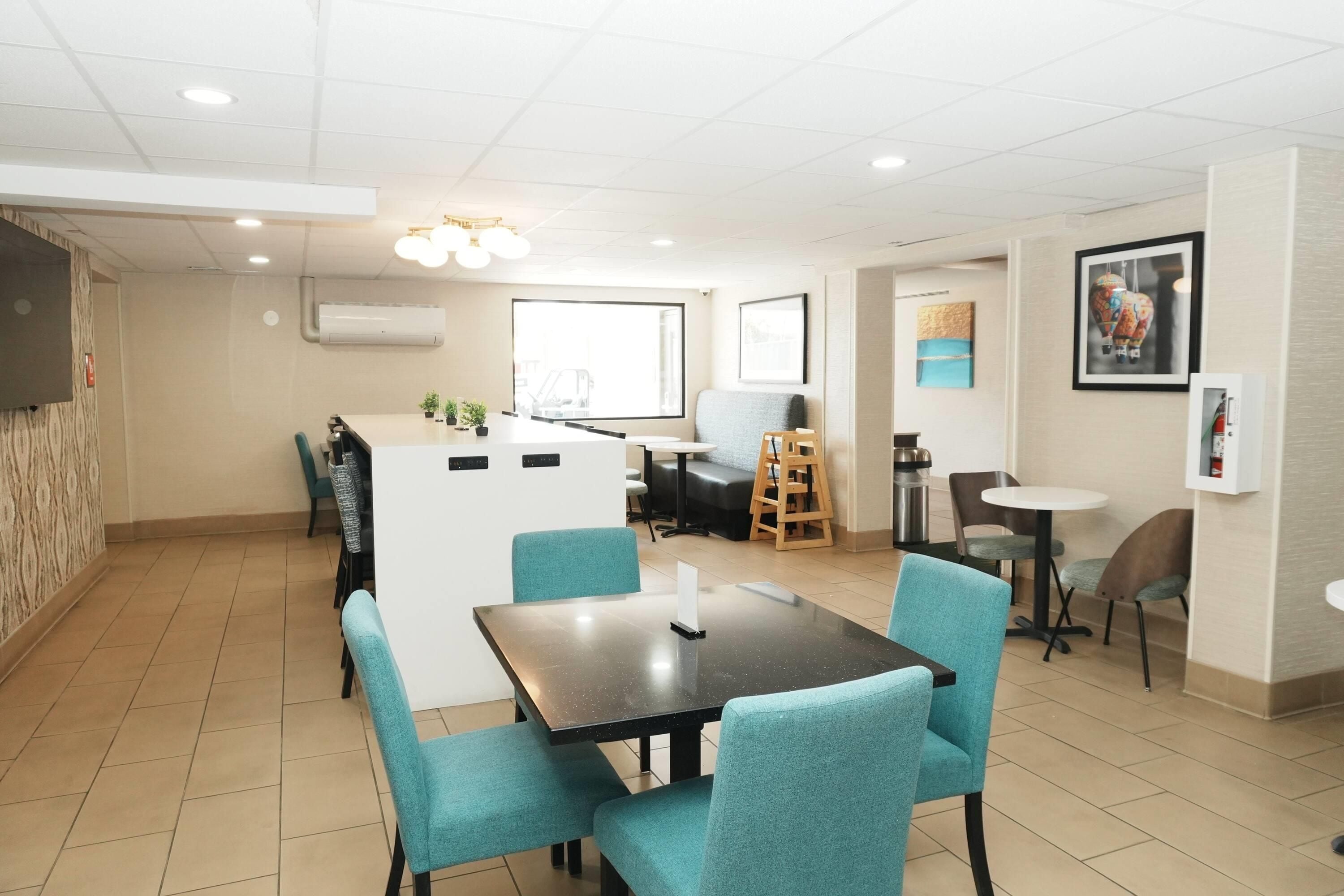 A modern hotel room with a dining area, a kitchenette, and a large window.