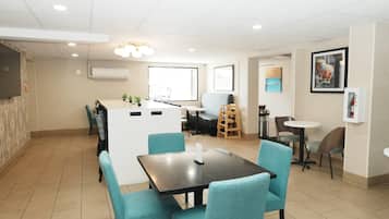 A modern hotel room with a dining area, a kitchenette, and a large window.