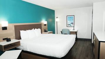 A hotel room with a bed, bedside tables, a desk, a chair, a desk lamp, and a framed picture on the wall.