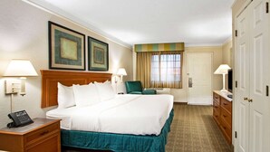 A hotel room with a large bed, two bedside lamps, a desk with a telephone, a chair, and a wardrobe. - La Quinta Inn by Wyndham Albuquerque Airport (Albuquerque)