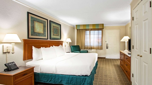 A hotel room with a large bed, two bedside lamps, a desk with a telephone, a chair, and a wardrobe. - La Quinta Inn by Wyndham Albuquerque Airport (Albuquerque)