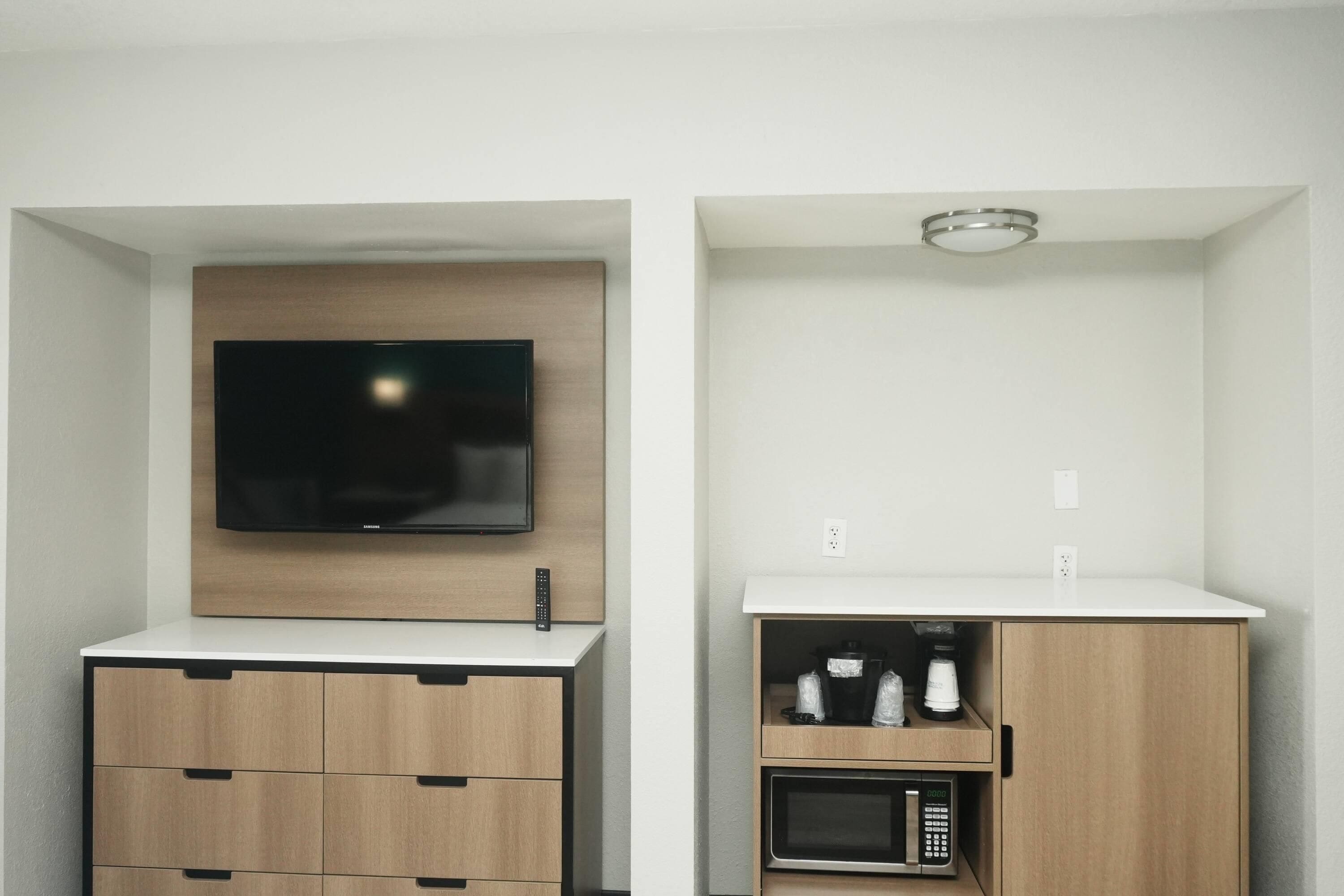 A modern kitchen with a built-in microwave, a coffee maker, and a TV mounted above a wooden cabinet.