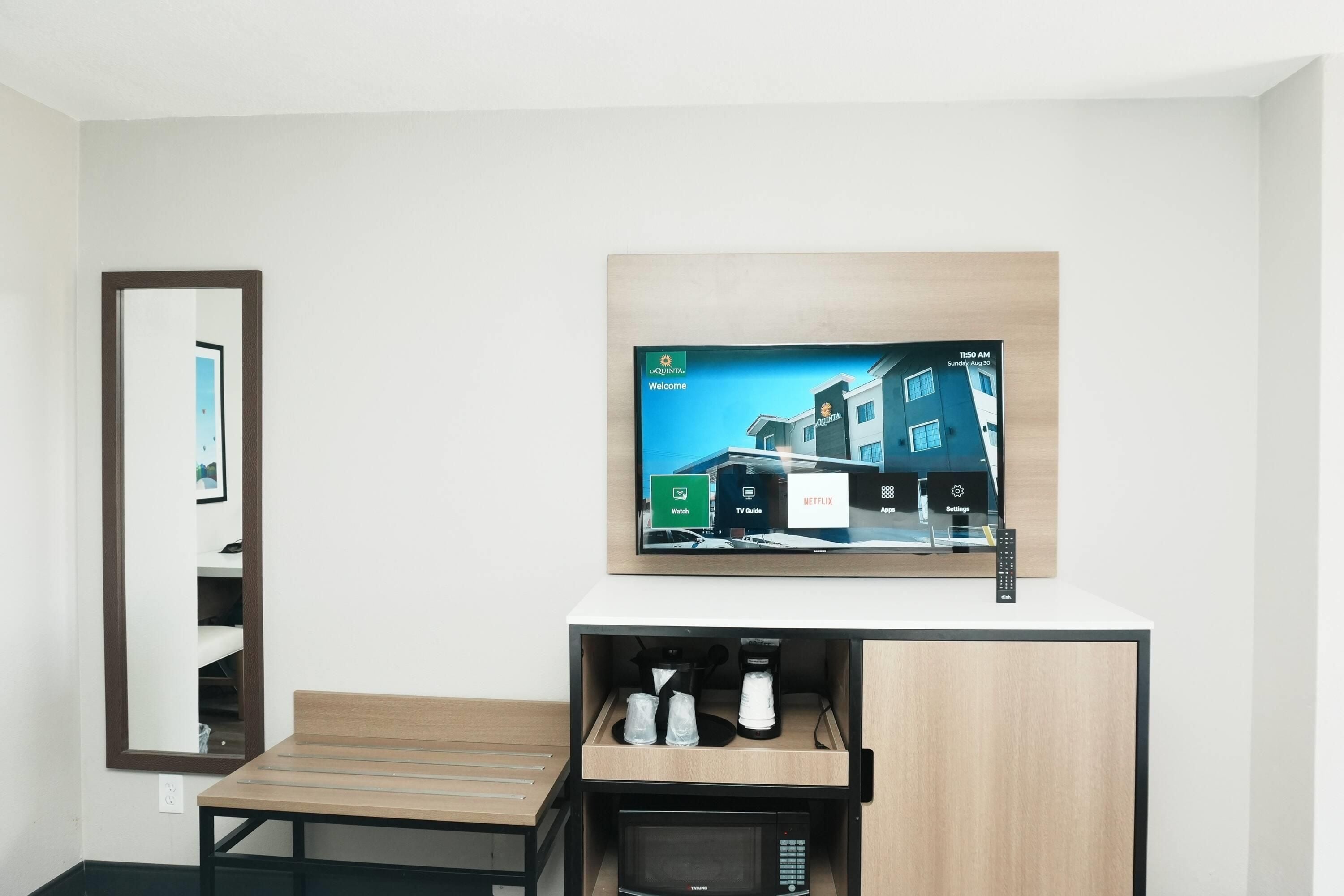 A hotel room with a bed, a TV mounted on the wall, and a small table with a remote control.