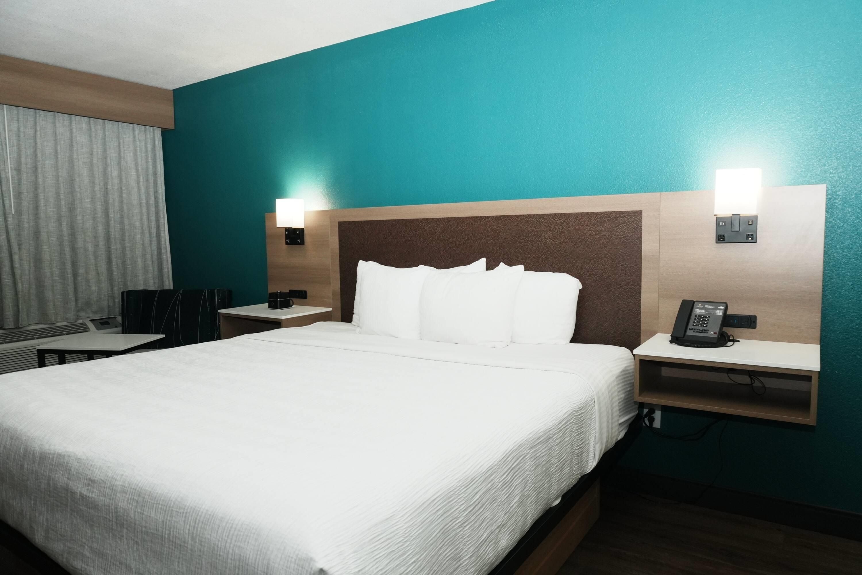 A hotel room with a large bed, a desk, a chair, and a nightstand with a phone.