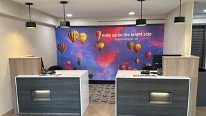 A reception area with two reception desks, a colorful mural with hot air balloons, and a 'La Quinta' doormat. - La Quinta Inn by Wyndham Albuquerque Airport (Albuquerque)