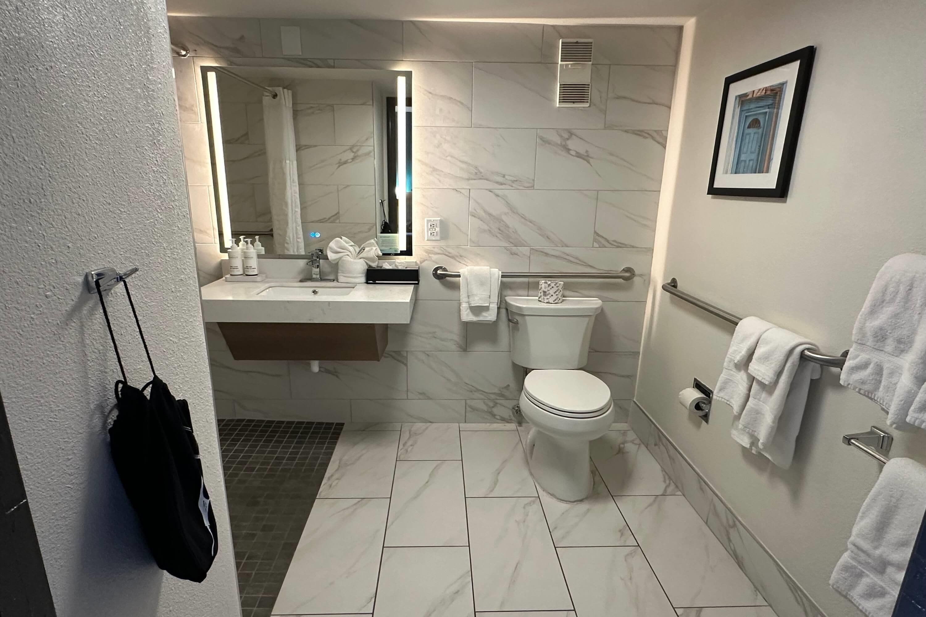 A modern bathroom with a marble floor, a sink with toiletries, a toilet, and a shower area.