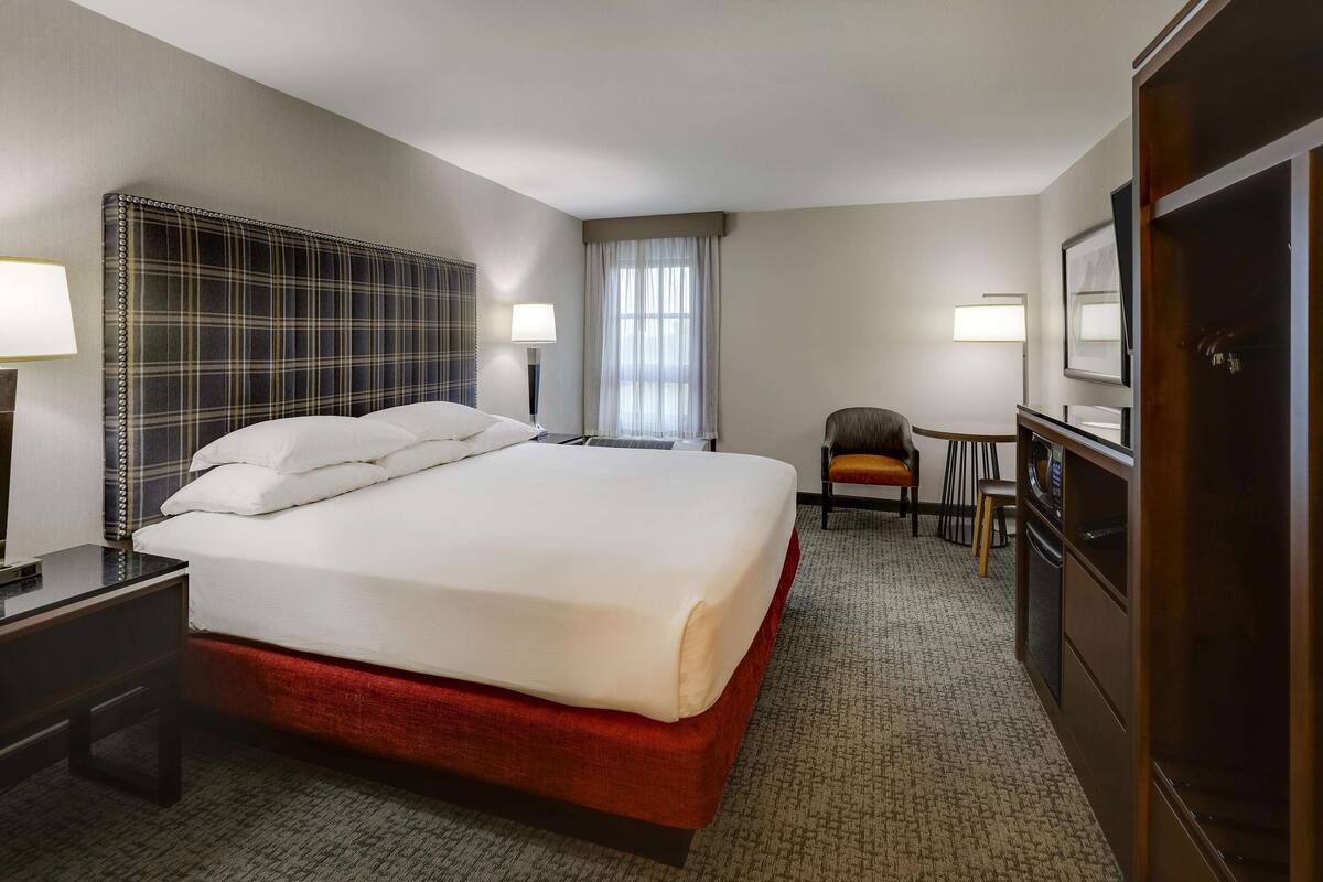 A hotel room with a large bed, a desk, a chair, a TV, and a wardrobe.